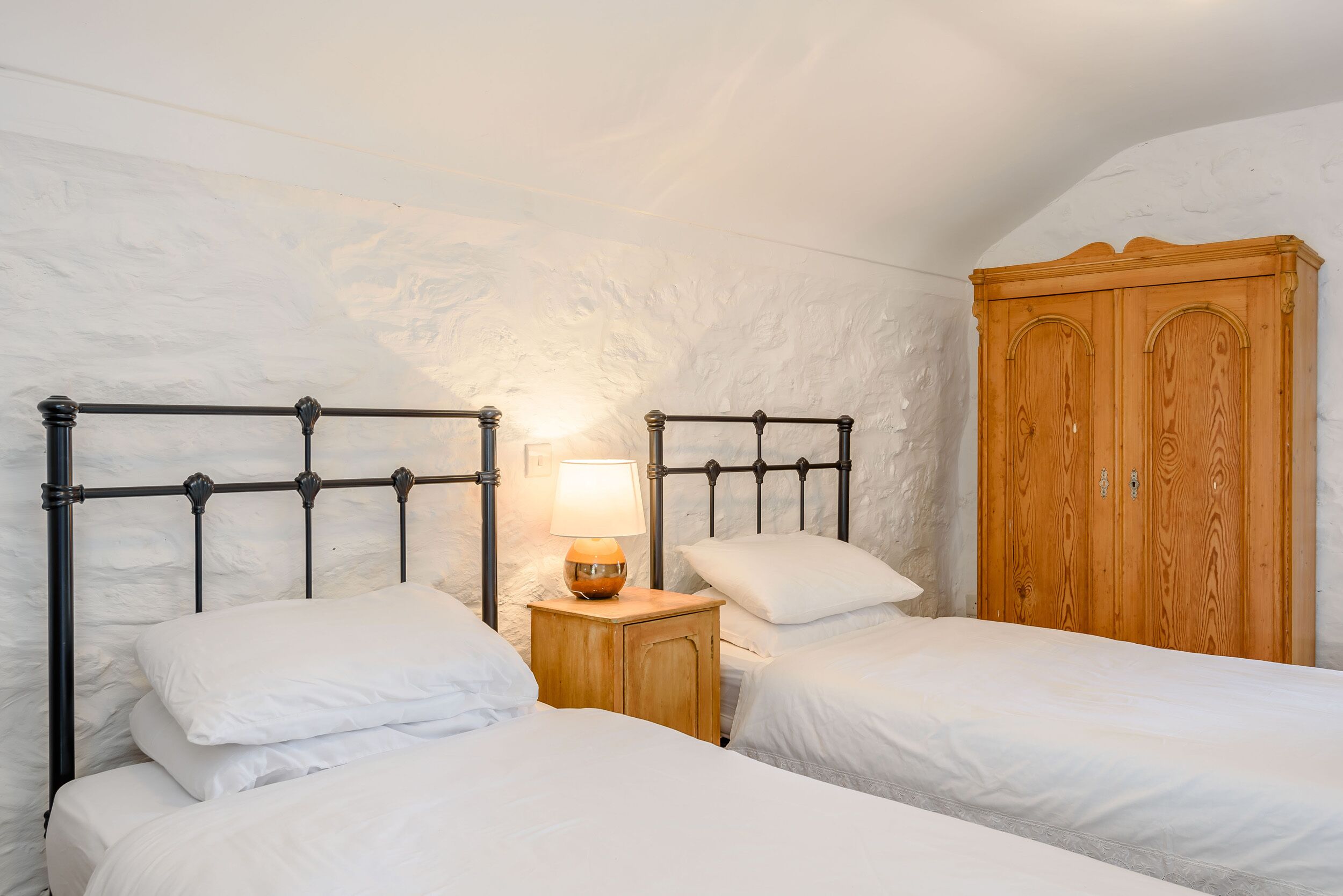 Quarto com duas camas, um guarda-roupa de madeira e uma mesa de cabeceira com abajur.