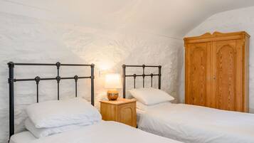 Quarto com duas camas, um guarda-roupa de madeira e uma mesa de cabeceira com abajur.