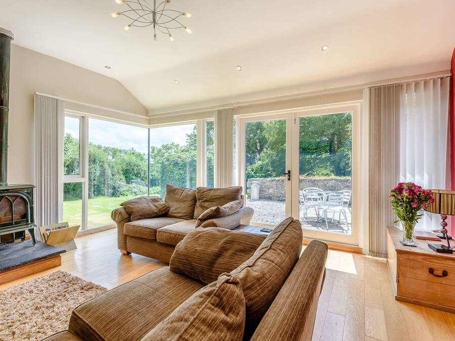 A spacious living room with a large sofa, a fireplace, and large windows offering a view of the outdoors.