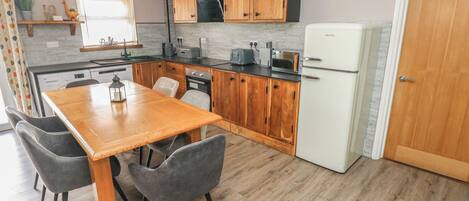 A compact kitchen with wooden cabinets, a white refrigerator, a dining table with chairs, and a microwave.