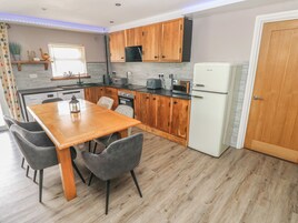 Cocina compacta con armarios de madera, un refrigerador blanco, una mesa de comedor con sillas y un microondas.