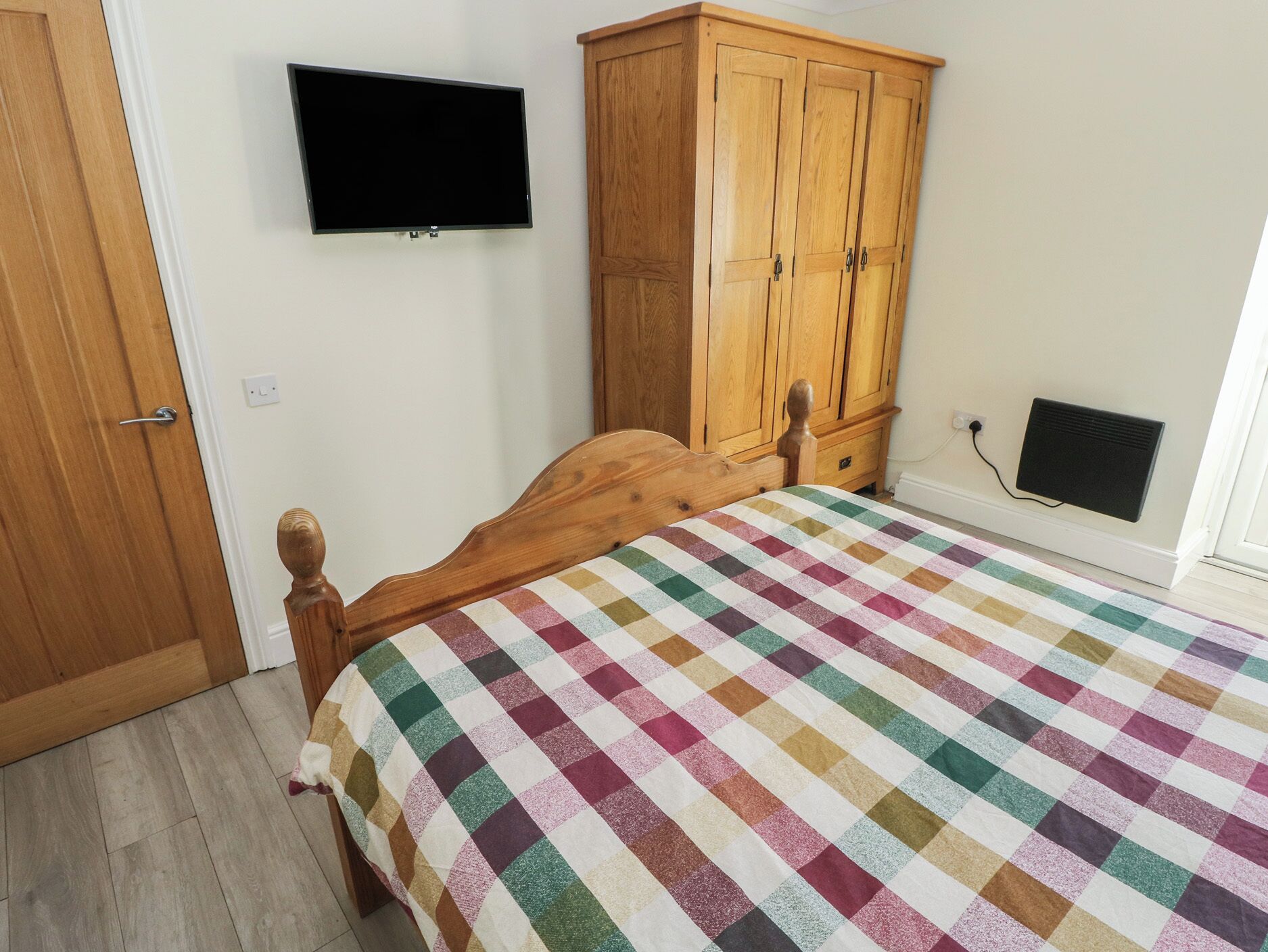 Een slaapkamer met een bed, een houten garderobe en een tv aan de muur.