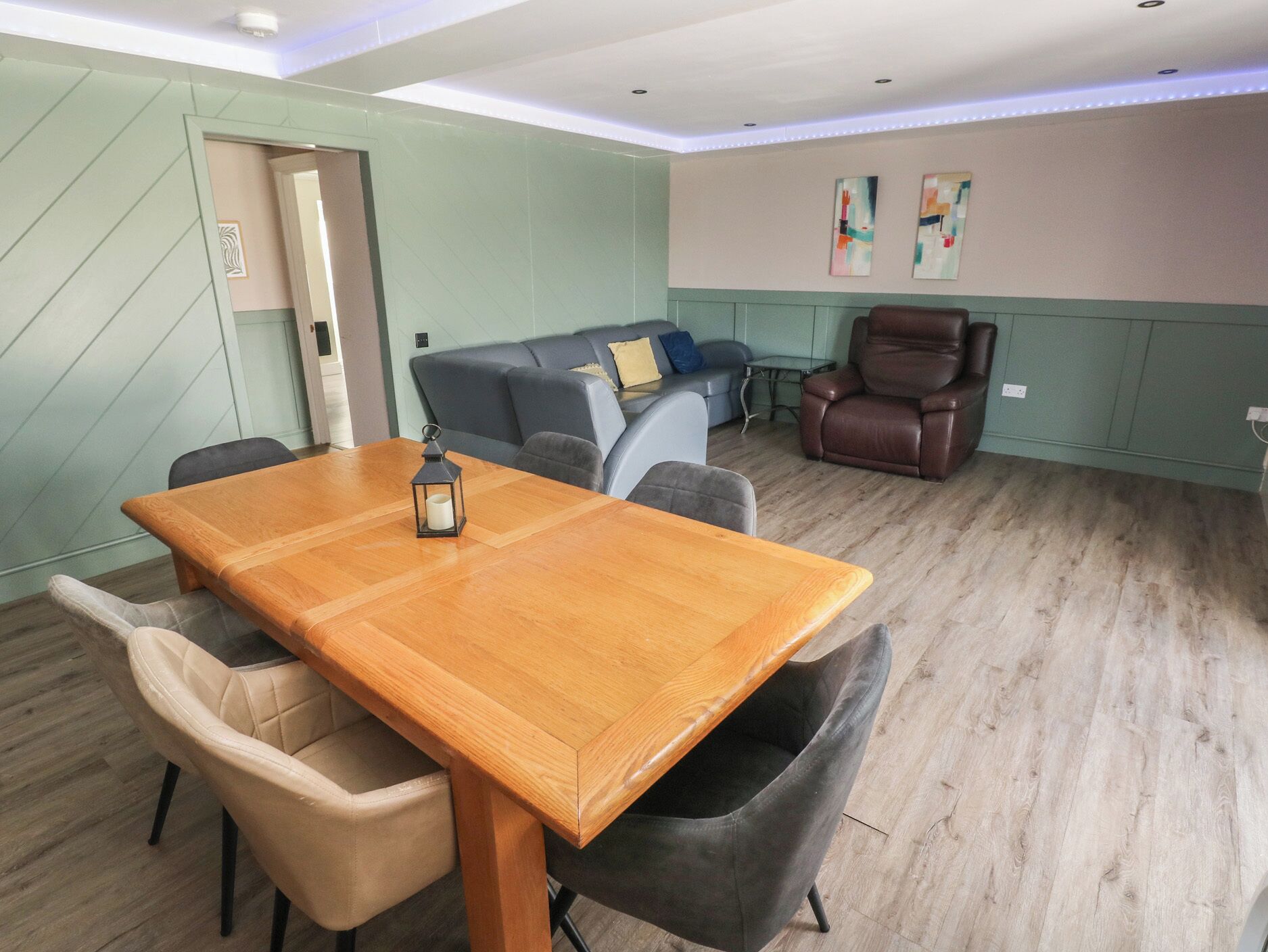 A conference room with a wooden table, two chairs, a sofa, a brown leather chair, and two abstract paintings on the wall.