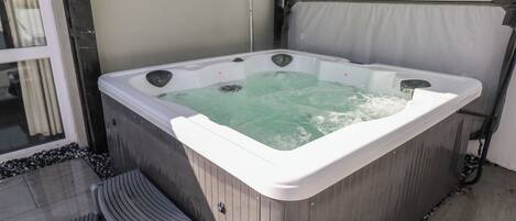 A hot tub with a wooden exterior, a step leading into it, and a glass door in the background.