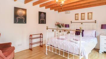 Una camera da letto con un letto con struttura in metallo bianco, travi in legno al soffitto, una sedia di legno e un divano rosa.