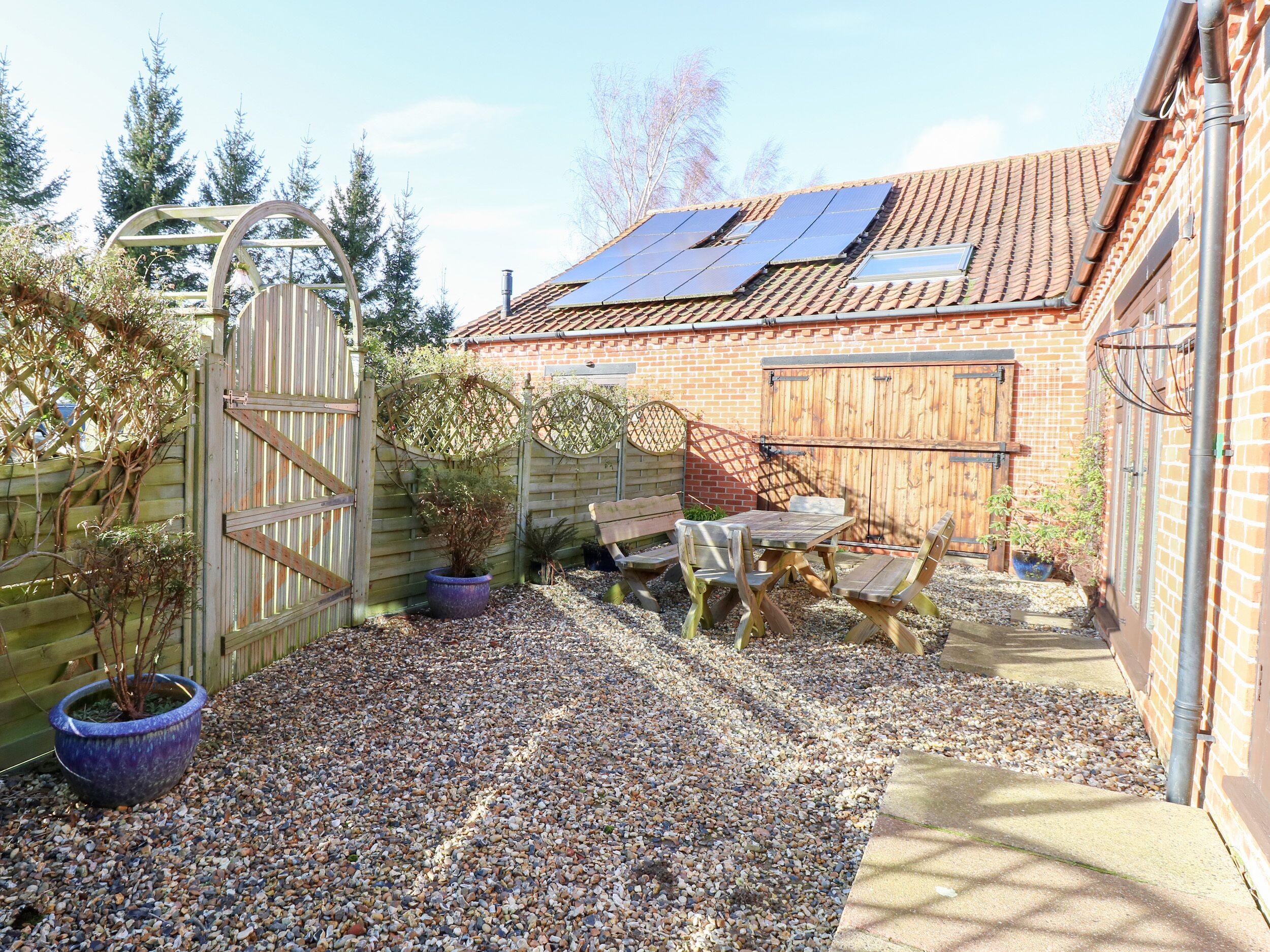 A backyard with a patio table and chairs, a wooden fence, a potted plant, and solar panels on the roof.