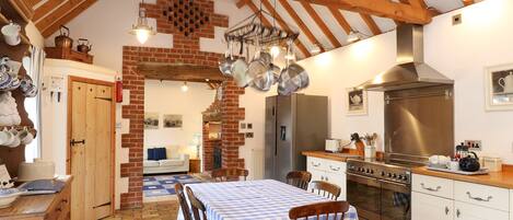A kitchen with a wooden ceiling, a brick wall, a dining table with chairs, and a stainless steel range hood.