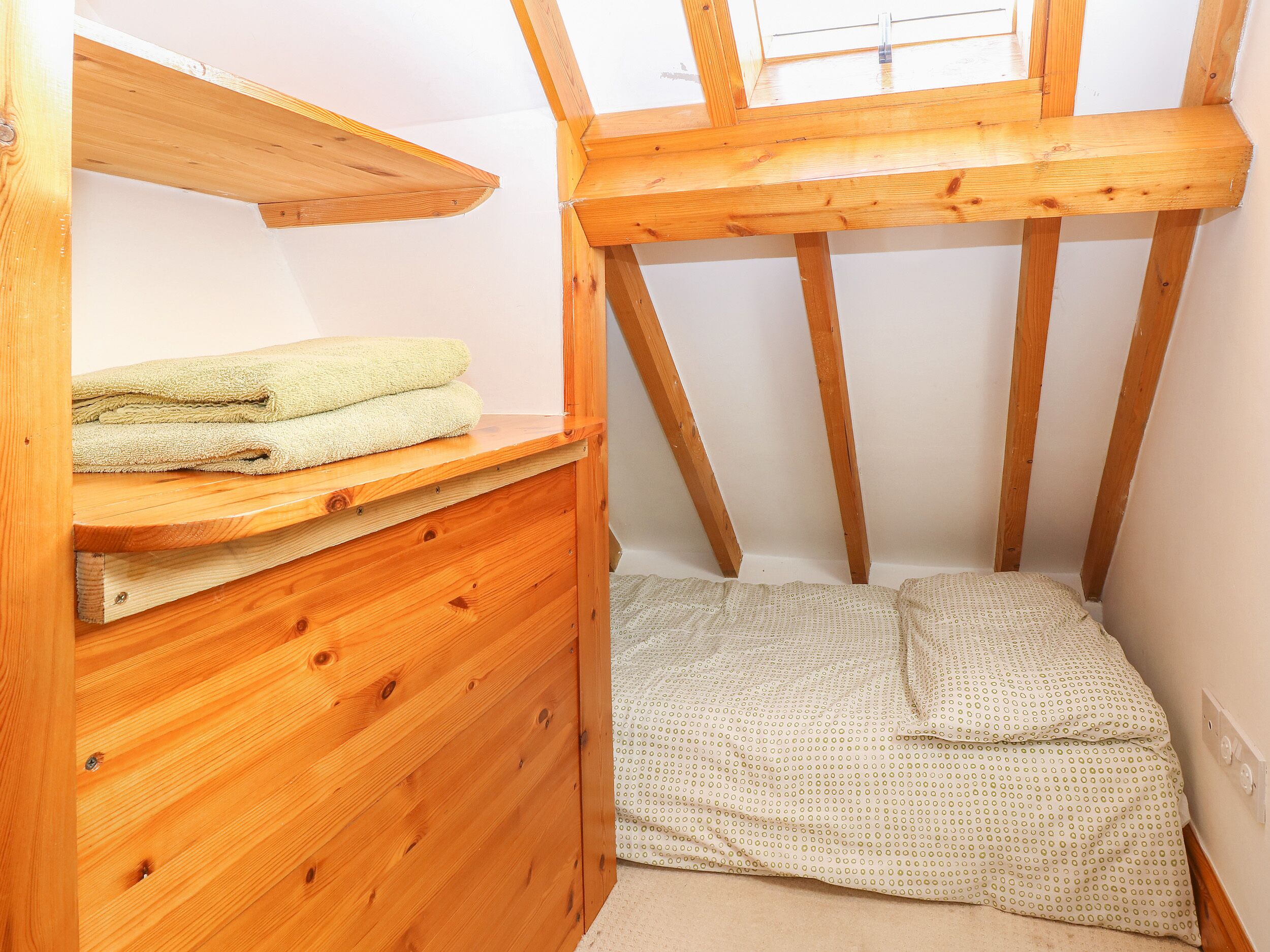 Un pequeño dormitorio en el ático con vigas de madera, un aparador de madera y una cama con colcha estampada.