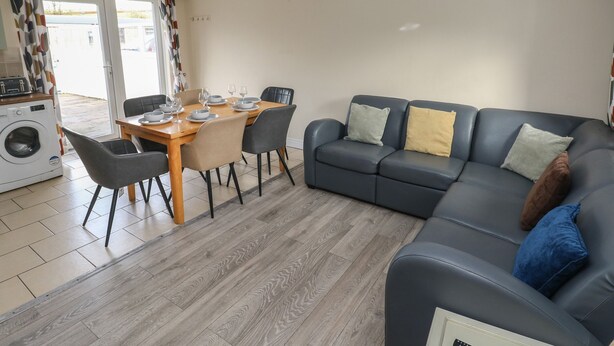 A modern living room with a dining area, a sofa set, and a washing machine. - Barn Cottage (Laugharne)
