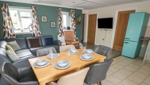 A modern living room with a dining area, a sofa set, a teal-colored refrigerator, and a flat-screen TV mounted on the wall. - Barn Cottage (Laugharne)