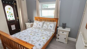 A bedroom with a wooden bed, a nightstand, a dresser, a radiator, and a door with a fire safety sign. - Barn Cottage (Laugharne)
