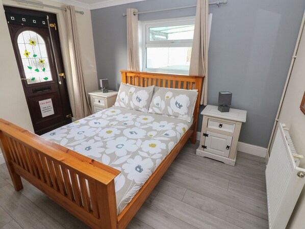 Un dormitorio con cama de madera, mesita de noche, cómoda, radiador y puerta con un letrero de seguridad contra incendios.