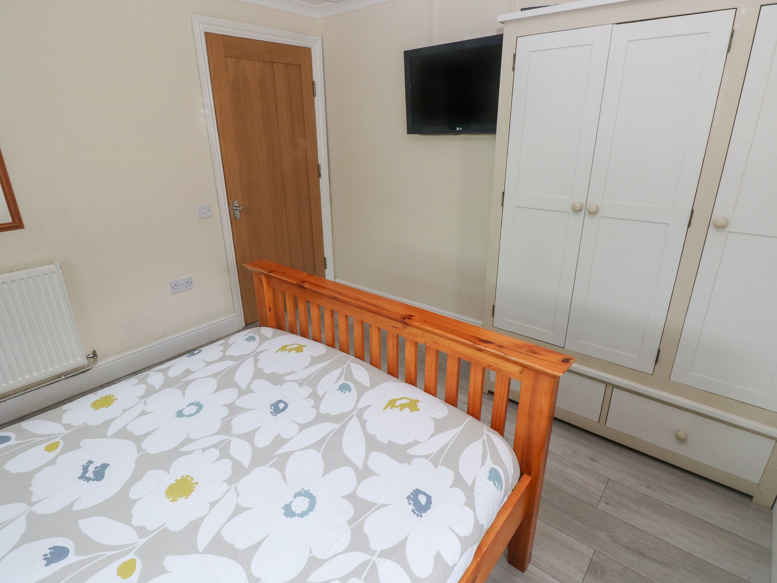 Un dormitorio con una cama de madera, un armario, un televisor y un radiador.