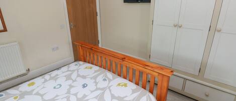 Un dormitorio con una cama de madera, un armario, un televisor y un radiador.