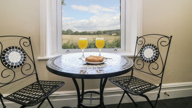 A small round table with two chairs, a window view of a field, and two glasses of orange juice. - Riverside View (Grange-over-Sands)