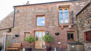 A stone building with a wooden door, a bench, and potted plants. - Swallow's Nest (Penrith)