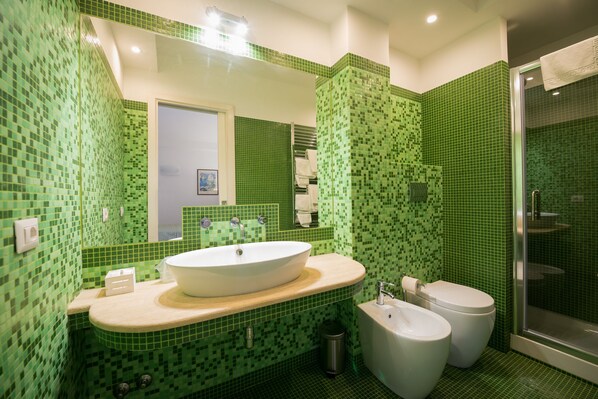 A bathroom with a large mirror, a sink, two toilets, and a shower area.
