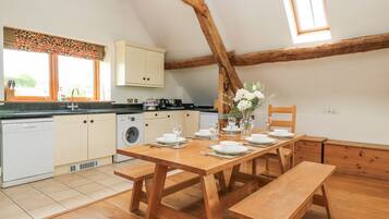 A cozy kitchen with wooden beams, a dining table set for four, and a washing machine.