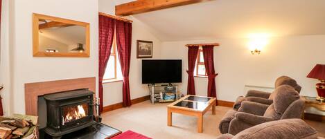 A cozy living room with a fireplace, comfortable seating, a television, and a wooden ceiling.