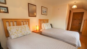 Une chambre avec deux lits, des têtes de lit en bois, une table de chevet avec une lampe, des tableaux encadrés au mur et une porte en bois.