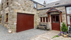Une petite maison en pierre avec une porte d’entrée en bois portant l’inscription « Poppy Cottage », un banc à l’extérieur et une allée gravillonnée.