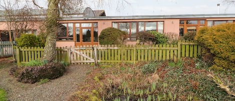 A building with a wooden fence, a pond with water plants, and a tree.