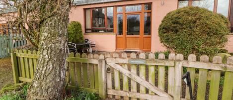 A pink building with a wooden gate, a tree, and a small garden.