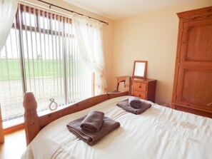 Een slaapkamer met een bed, twee handdoeken, een houten dressoir, een spiegel en een raam met gordijnen.