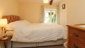 Une chambre à coucher avec un lit, une table de chevet, une commode, une lampe et une fenêtre avec des rideaux.