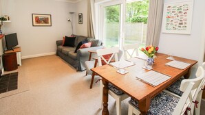 A cozy living room with a sofa, a dining table set for two, and a large window with curtains. - Inglenook (Ludlow)