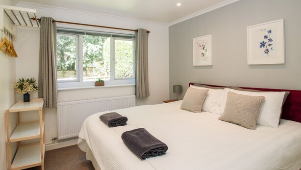A neatly arranged bedroom with a large bed, a bedside table, a radiator, and a window with curtains. - Inglenook (Ludlow)
