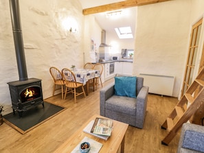 A cozy living room with a fireplace, wooden furniture, a dining area, and a kitchen in the background.