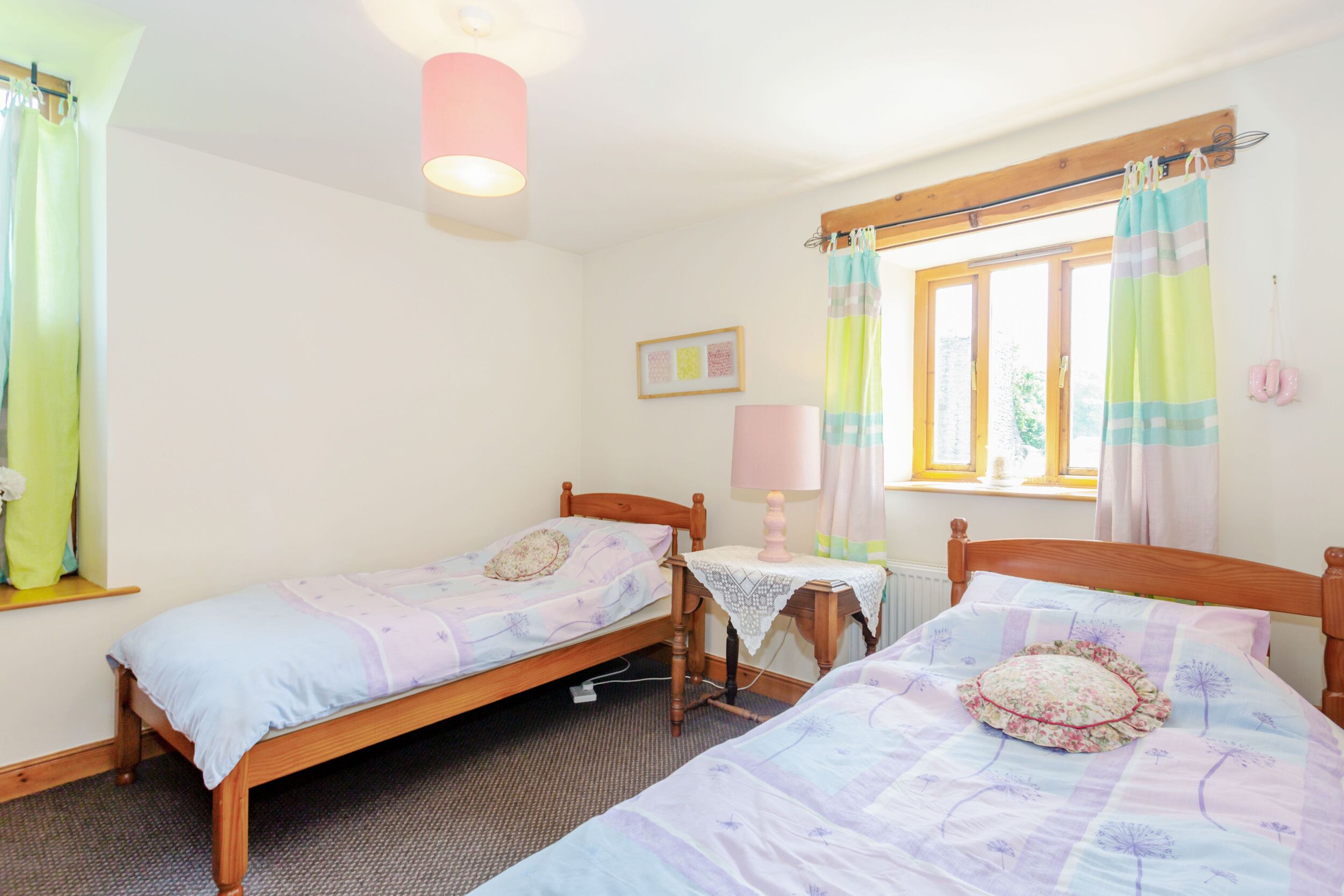 A room with two single beds, a small table, a lamp, and a window with curtains.