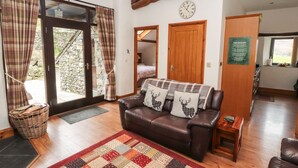 A cozy living room with a brown leather sofa, a patterned rug, and plaid curtains. - The Hayloft (Keswick)