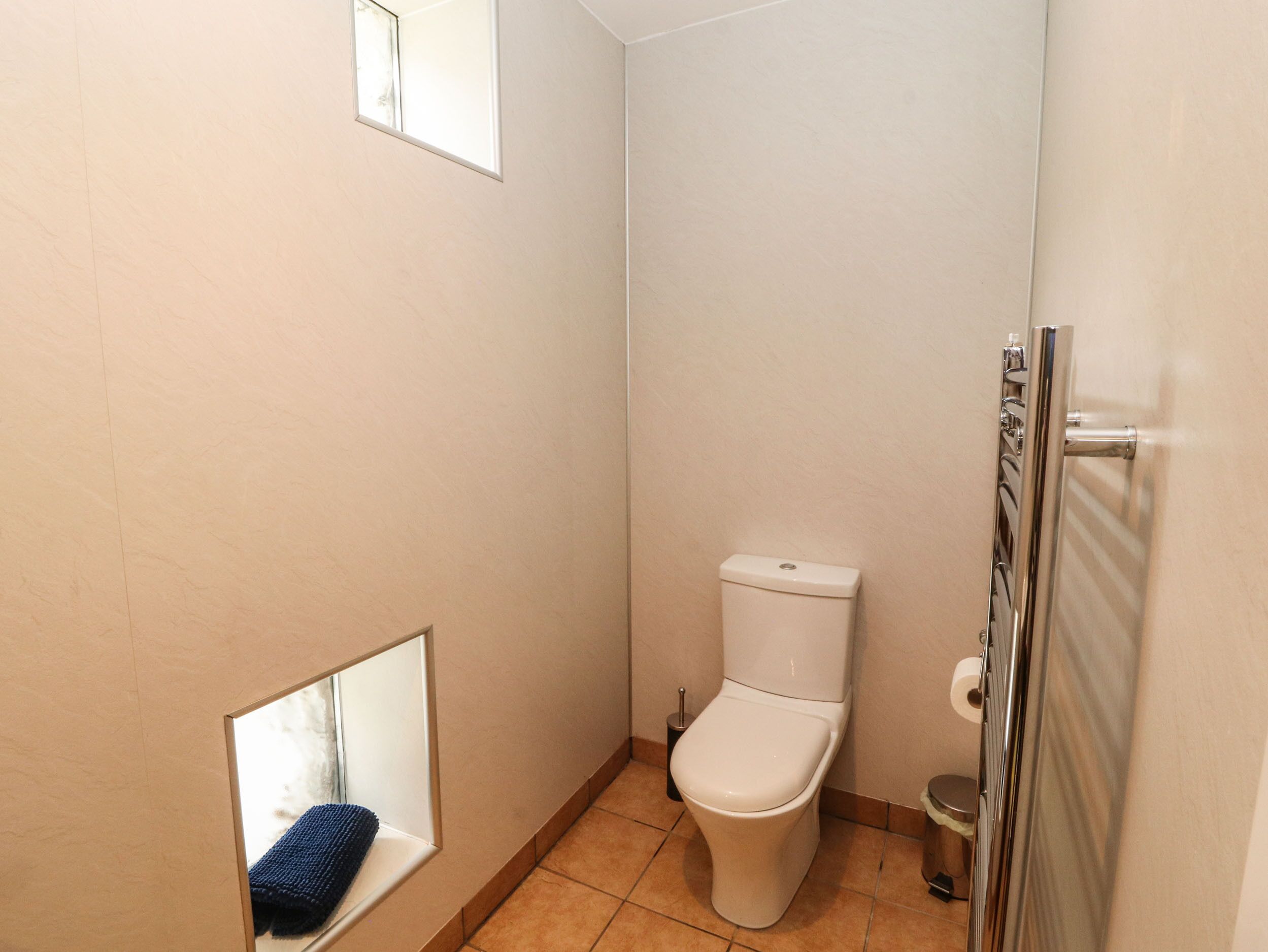 A small bathroom with a toilet, a mirror, and a towel rack.