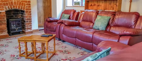 A cozy living room with a brick fireplace, leather sofa, wooden cabinet, and a floral carpet.