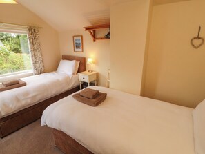 A hotel room with two beds, a nightstand with a lamp, a framed picture on the wall, and a heart-shaped decoration.
