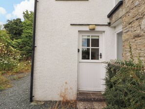 A white door with a window, a small step leading up to it, and a stone wall to the right.