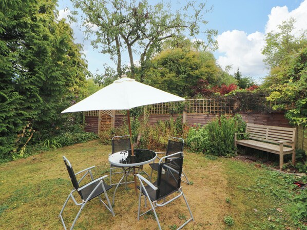An outdoor seating area with a round table and chairs, a white umbrella, and a wooden bench.