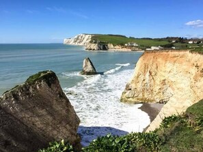 A coastal landscape with cliffs, a prominent rock formation, and a view of the sea. - Hill Farm Cottage (Freshwater)