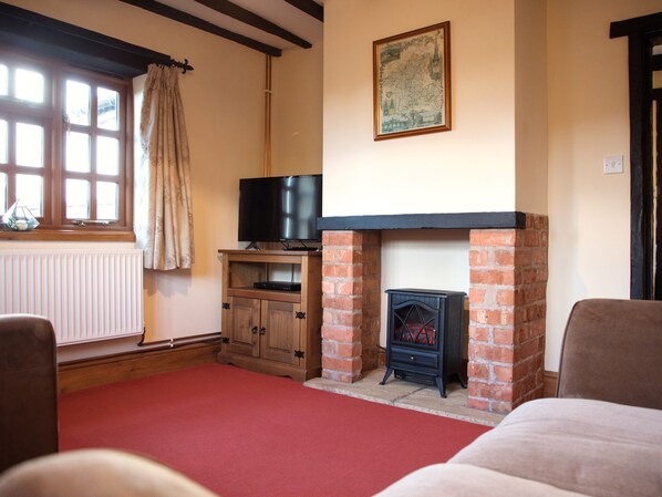 A living room with a fireplace, a television on a wooden stand, and a red carpet. - Yew Tree Cottage (Malvern)