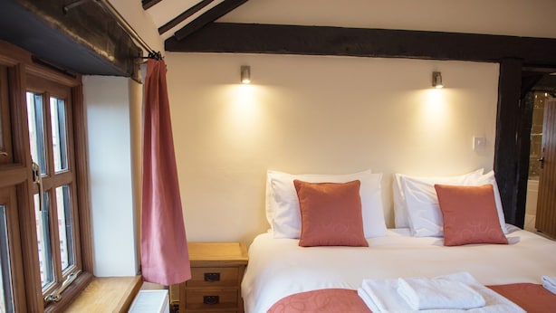 Ein Hotelzimmer mit einem großen Bett, Nachttischen aus Holz, einem Fenster mit Vorhängen und einer Heizung.