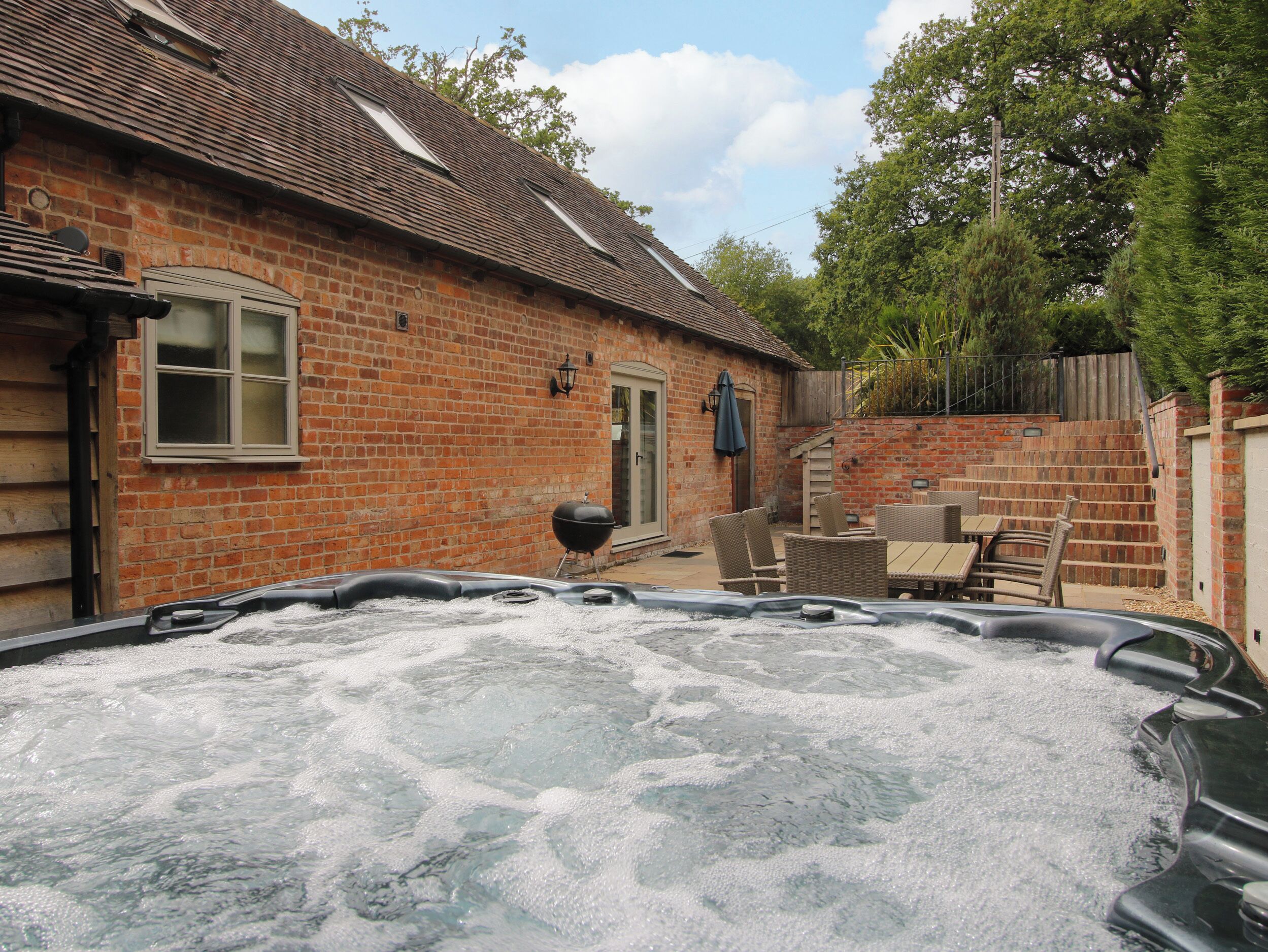 A hot tub in a backyard with a brick house, outdoor furniture, and a wooden fence.