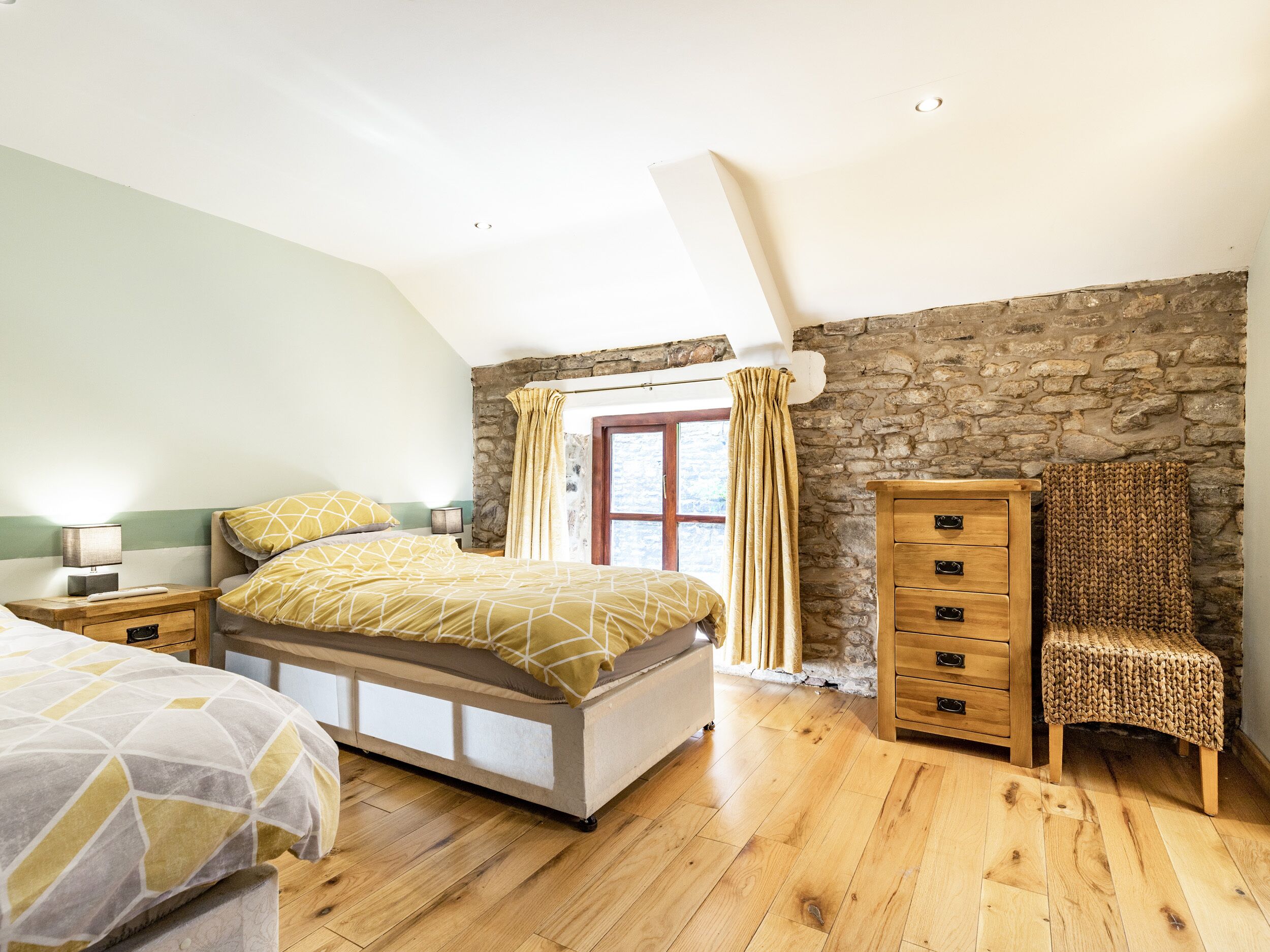 A bedroom with a bed, wooden nightstands, a dresser, a chair, and a stone wall.