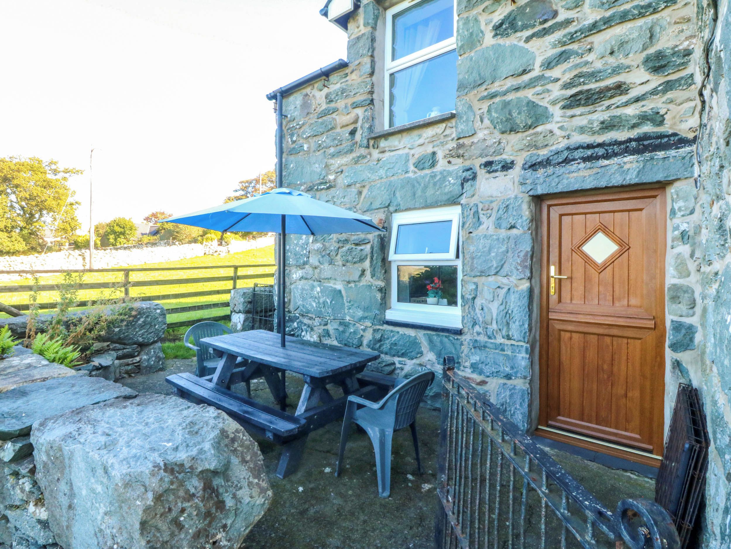 A stone building with a wooden door, a window, and a picnic table with an umbrella.