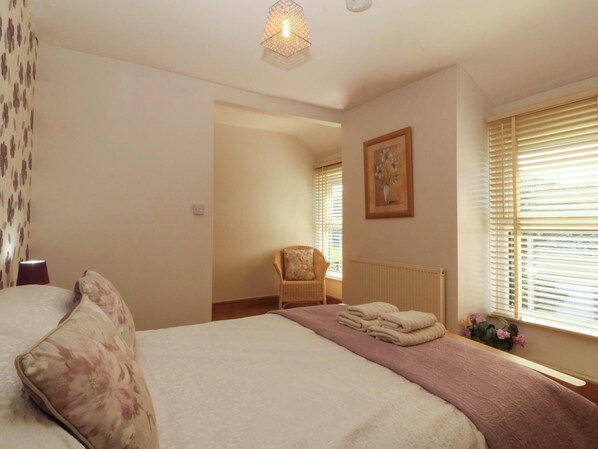A bedroom with a bed, a chair, a radiator, and a window with blinds. - Tyddyn (Dyffryn Ardudwy)