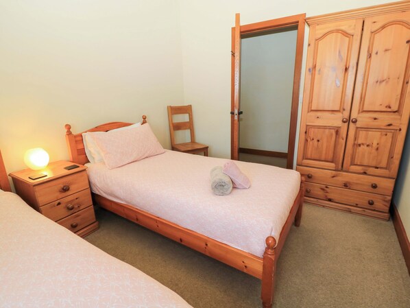 Un dormitorio con una cama de madera, una mesita de noche con una lámpara, una silla y un armario.