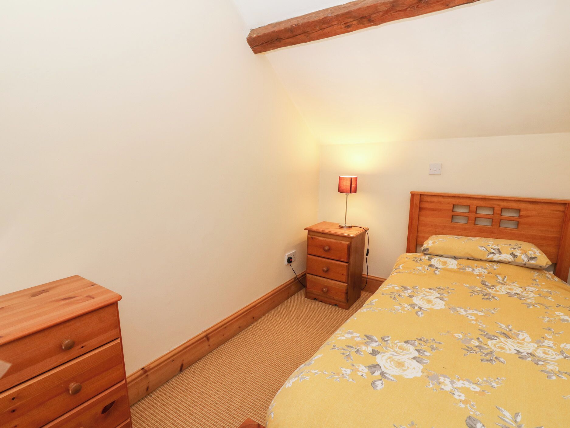 Un dormitorio con una cama de madera, una mesita de noche con lámpara y un aparador de madera.