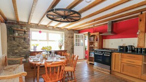 A cozy kitchen with wooden floors, a dining area with a round table and chairs, and a stone wall. - The Farmhouse (Lampeter)