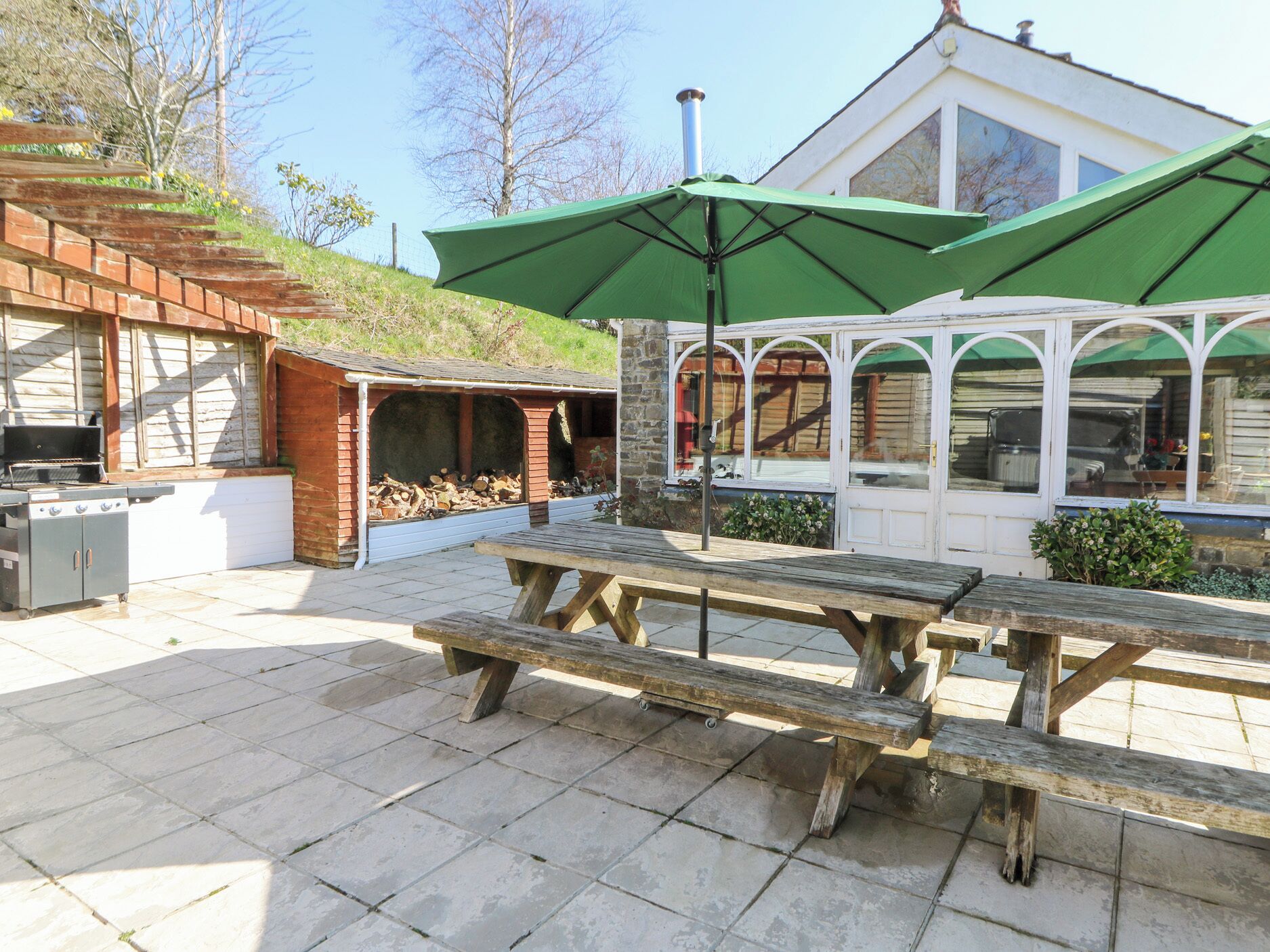 An outdoor patio with a barbecue grill, a covered seating area, and a stone-tiled floor.